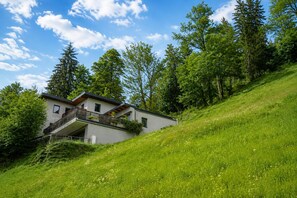 Een modern huis met een balkon, omringd door weelderig groen en bomen.