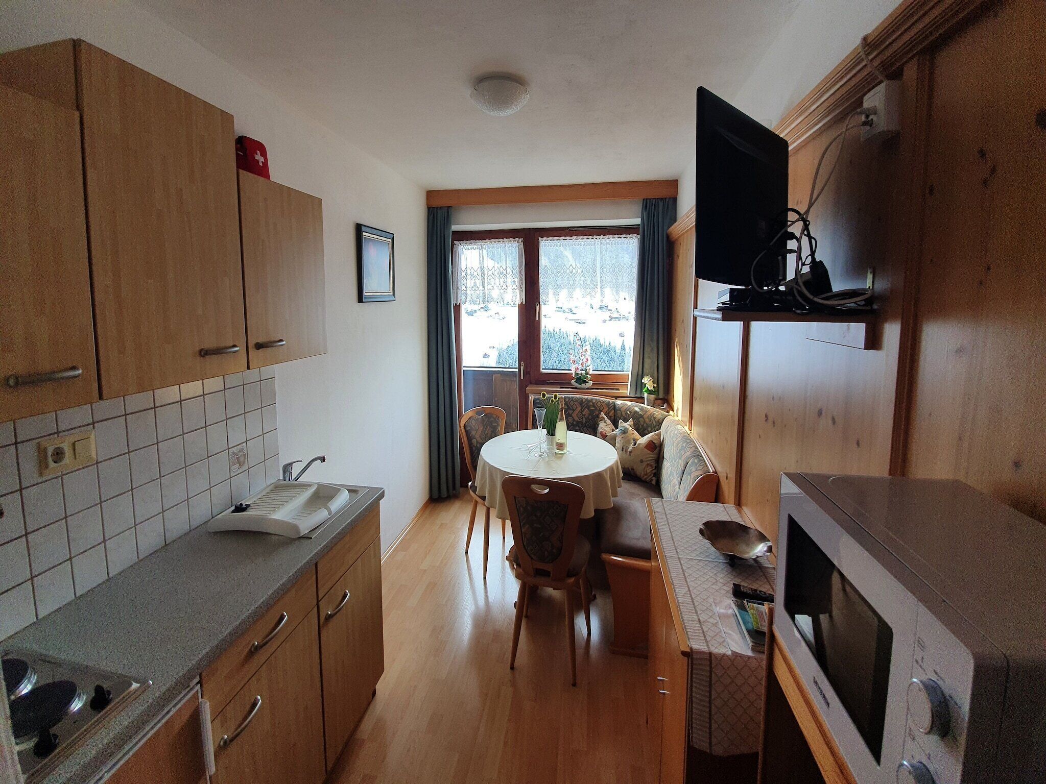 A compact kitchen with wooden cabinets, a built-in microwave, and a dining area with a round table and chairs.