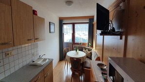 A compact kitchen with wooden cabinets, a built-in microwave, and a dining area with a round table and chairs. - Apartment in Gerlosberg near Ski Lift (Zell am Ziller-Gerlosberg)
