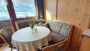 A cozy room with a round table, wooden chairs, a cushioned bench, and a window with a view of a snowy landscape. - Apartment in Gerlosberg near Ski Lift (Zell am Ziller-Gerlosberg)