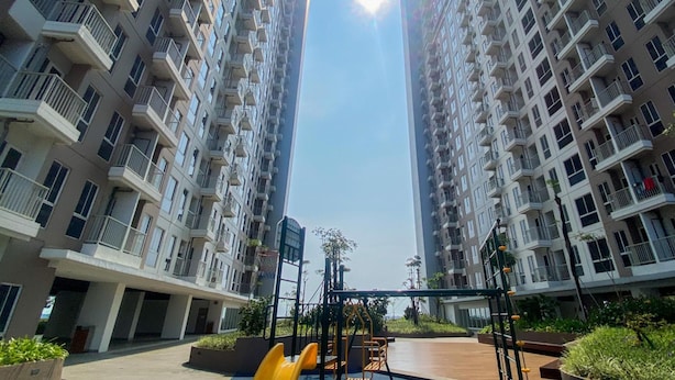 A high-rise residential building with multiple balconies, a playground, and a clear sky. - Cozy And Restful Studio Tokyo Riverside Pik 2 Apartment (Teluknaga)