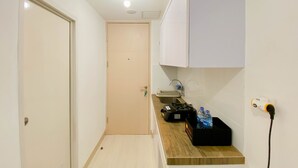 A narrow hallway with a door at the end, a countertop with a kettle, a water dispenser, and a black box. - Cozy And Restful Studio Tokyo Riverside Pik 2 Apartment (Teluknaga)