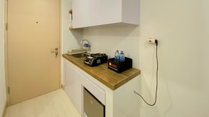 A small kitchenette with a sink, a stove, and a cabinet above it. There is a black box with water bottles on the counter. - Cozy And Restful Studio Tokyo Riverside Pik 2 Apartment (Teluknaga)