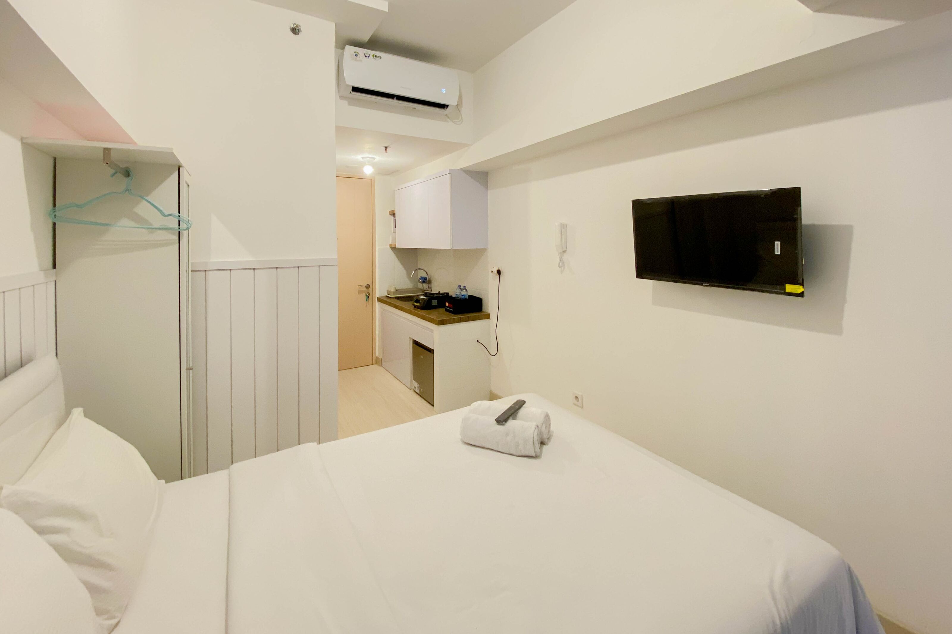 Une chambre d’hôtel avec un lit, un téléviseur fixé au mur, une kitchenette et une salle de bain où une serviette est accrochée à la porte.