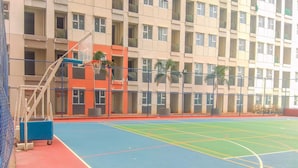 Una cancha de baloncesto cubierta con piso azul y rojo, rodeada por una valla alta.