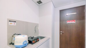 Una kitchenette pequeña con un lavamanos, una cafetera y un dispensador de agua. Hay un cartel en la pared y una puerta con cerradura de seguridad.