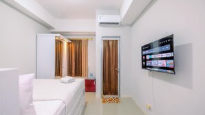 Habitación de hotel con cama, televisor montado en la pared, equipo de aire acondicionado y una puerta con cortinas.