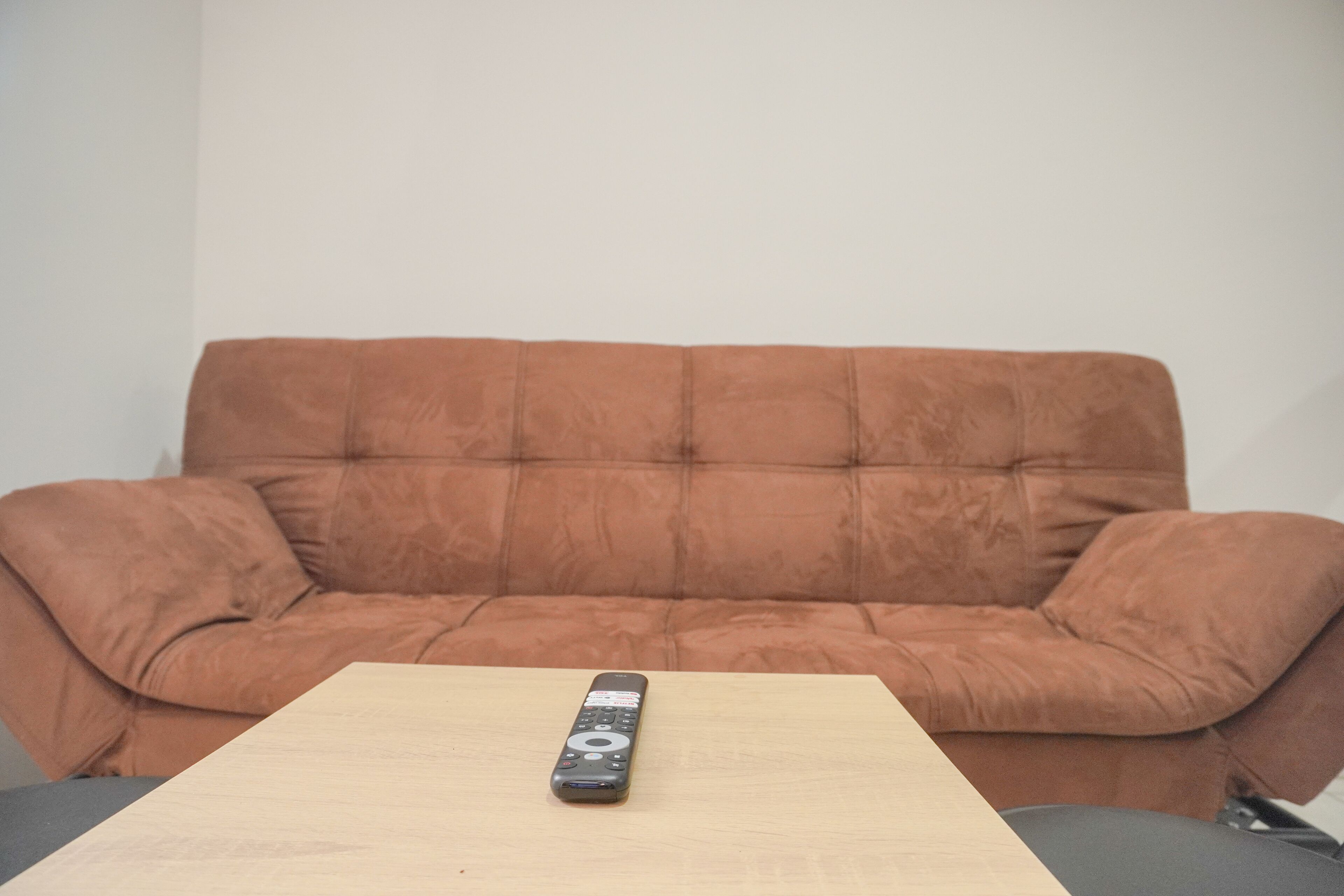 A remote control on a wooden table in front of a brown sofa.