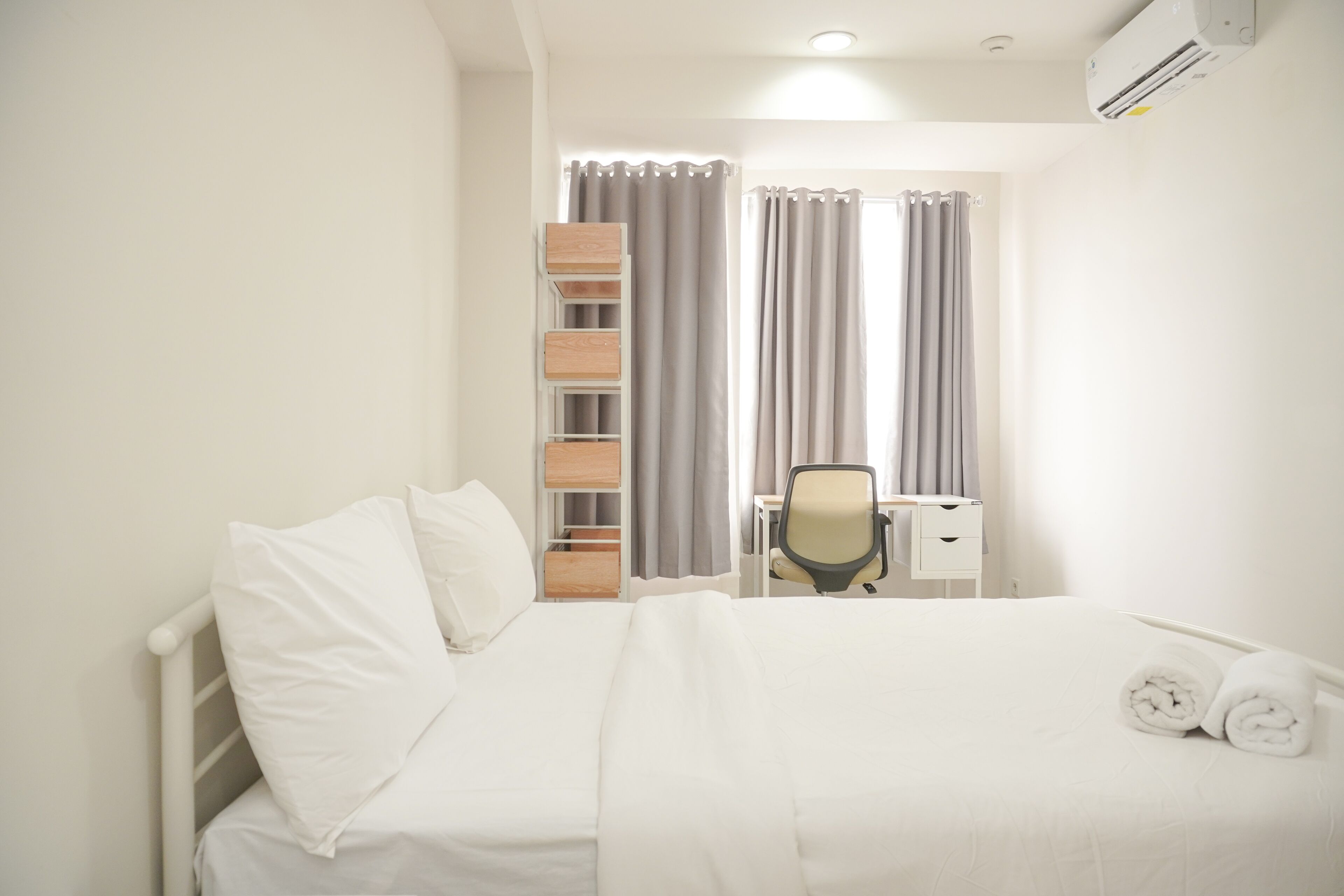 A hotel room with a bed, a desk, a chair, and a shelf unit.