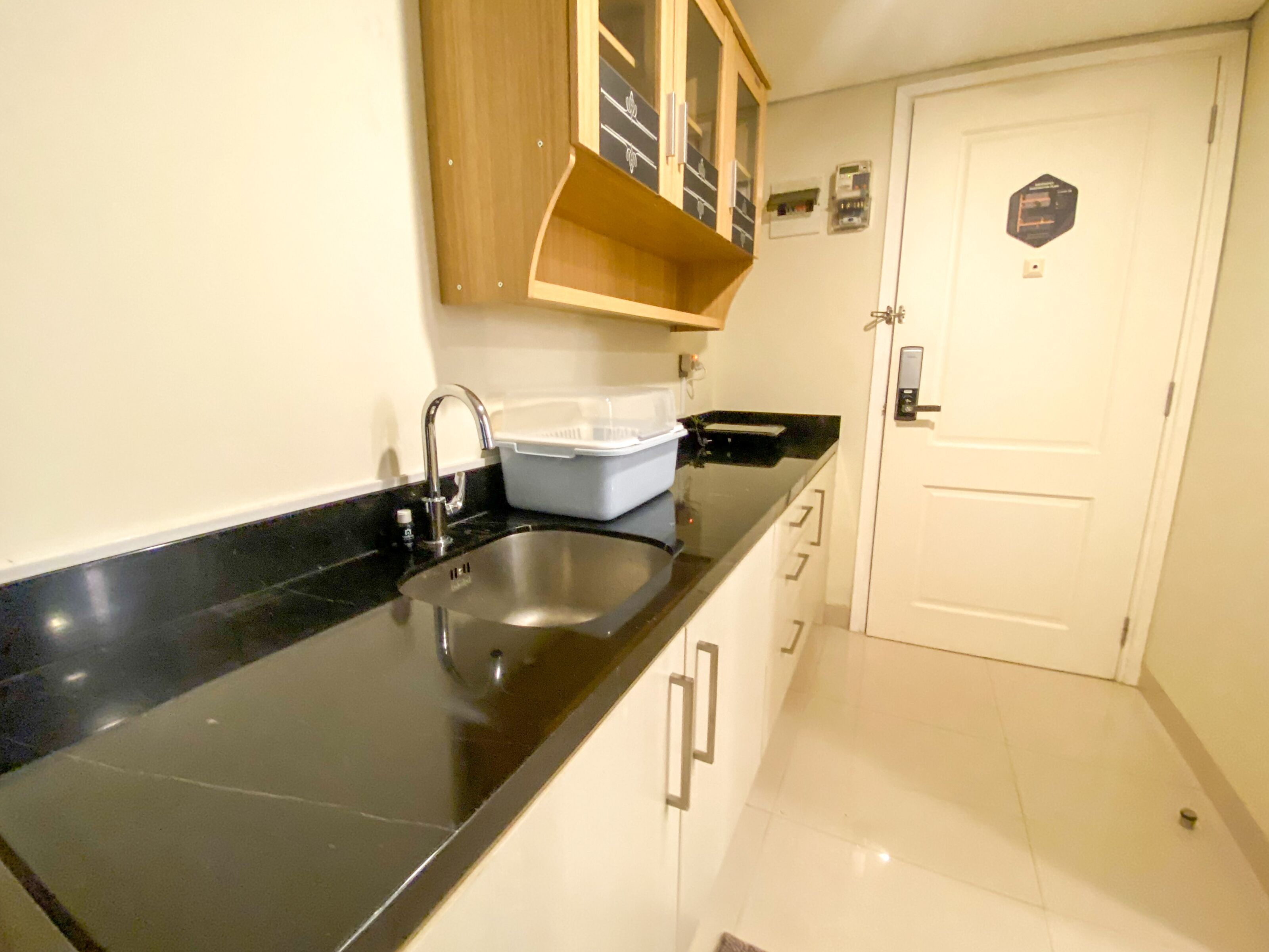 A kitchen with a black countertop, stainless steel sink, wooden cabinets, and a white door.