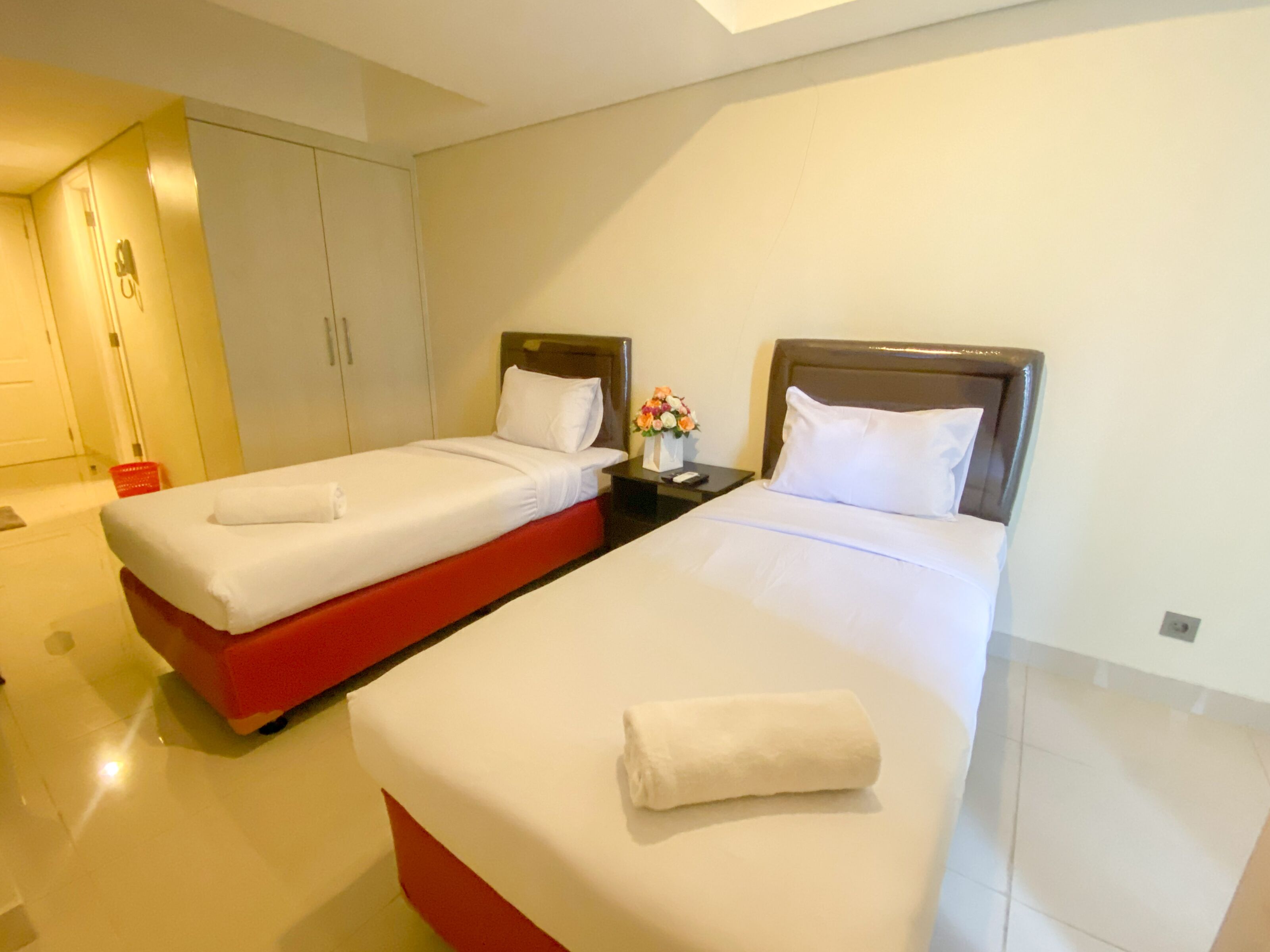 Una habitación de hotel con dos camas, un armario y una mesita de noche con un florero.