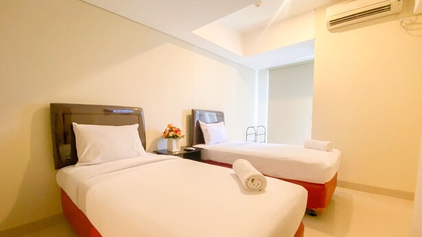 A hotel room with two beds, each with white bedding and a wooden headboard. There is a small table with a vase of flowers between the beds. - Minimalist Studio Room Marquis De Lafayette Apartment (Semarang)