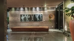 A modern lobby with a wooden bench, a wall-mounted cactus art piece, and a potted plant. - Comfortable And Homey 1Br At Uttara The Icon Apartment (Depok)