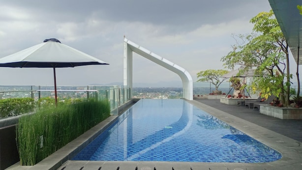 A swimming pool with a view of the city, surrounded by greenery and a modern architectural structure. - Comfortable And Homey 1Br At Uttara The Icon Apartment (Depok)
