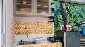A compact kitchen with a tiled backsplash, a sink, a stove, and a refrigerator. - Warm And Cozy Stay Studio Green Bay Pluit Apartment (Jakarta)