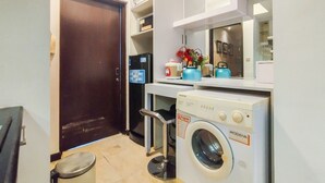 A compact kitchen with a washing machine, a refrigerator, and a microwave. - Best Location 1Br Without Living Room Apartment Braga City Walk (Bandung)