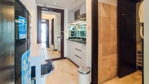 A modern kitchen with white cabinets, a stainless steel sink, and a black countertop. There is a trash can and a door leading to another room. - Best Location 1Br Without Living Room Apartment Braga City Walk (Bandung)