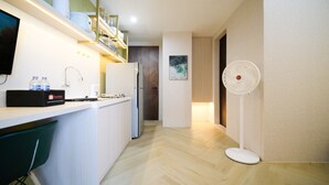Eine moderne Küche mit weißer Arbeitsplatte, Spüle und eingebautem Backofen. In der Ecke steht ein weißer Ventilator und ein grüner Stuhl.