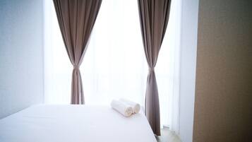 A hotel room with a bed, two curtains, and a rolled towel on the bed.