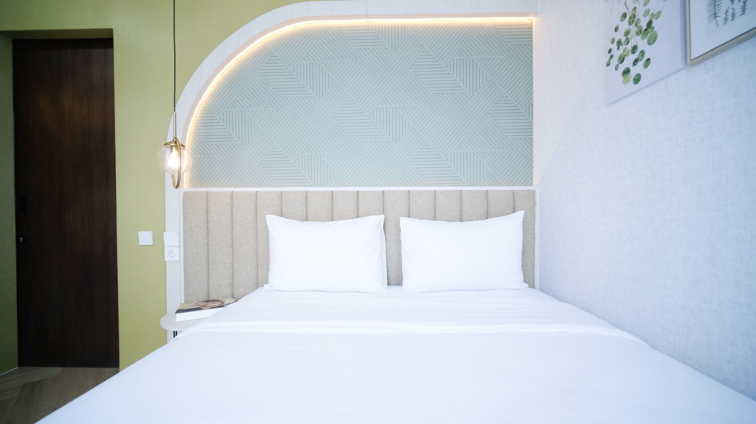 A hotel room with a bed, a headboard with a geometric pattern, a light fixture, and a door.