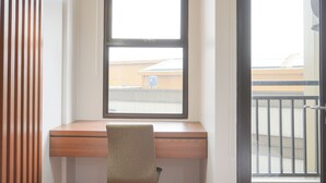 Une pièce avec un bureau en bois, une chaise et une fenêtre donnant sur des bâtiments.