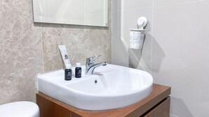 Une salle de bain avec un lavabo blanc, deux articles de toilette, un miroir et un distributeur de savon fixé au mur.