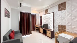 A modern hotel room with a seating area, a desk, and a television. - Spacious 2Br At Delft Ciputra Makassar Apartment (Makassar)