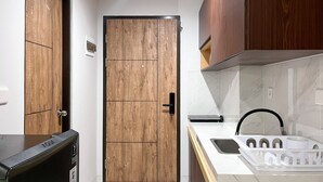 A compact kitchen with wooden cabinets, a built-in dishwasher, a sink with a black faucet, and a countertop with a white dish rack. - Spacious 2Br At Delft Ciputra Makassar Apartment (Makassar)