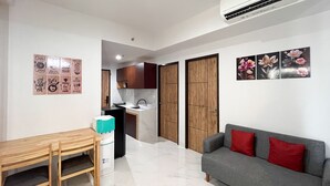 A compact living space with a dining area, kitchenette, and a sofa with red cushions. - Spacious 2Br At Delft Ciputra Makassar Apartment (Makassar)