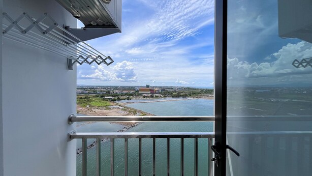 A balcony with a metal railing overlooking a body of water and a distant landscape. - Spacious 2Br At Delft Ciputra Makassar Apartment (Makassar)