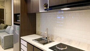 A modern kitchen with dark wood cabinets, a white tiled backsplash, a built-in microwave, and a black induction cooktop. - Elegant And Comfort 1Br Sudirman Suites Apartment (Jakarta)