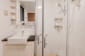 A modern bathroom with a glass-enclosed shower, a white sink, and a mirror above the sink. - Homey And Spacious 3Br Sky House Bsd Apartment (Pagedangan)