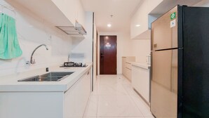 A modern kitchen with a stainless steel sink, a black refrigerator, and a wooden door in the background. - Homey And Spacious 3Br Sky House Bsd Apartment (Pagedangan)