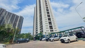 A tall residential building with multiple balconies, a parking area with several cars, and a green pedestrian bridge. - Homey And Spacious 3Br Sky House Bsd Apartment (Pagedangan)