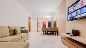 A modern living room with a sofa, a dining area with chairs, a TV mounted on the wall, and a kitchen in the background. - Homey And Spacious 3Br Sky House Bsd Apartment (Pagedangan)