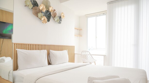Moderni hotellihuone, jossa on puinen sängynpääty, valkoiset vuodevaatteet, litteänäyttöinen televisio ja suuri ikkuna, jossa on sälekaihtimet.