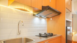 A compact kitchen with a stainless steel sink, a gas stove, wooden cabinets, and a white tiled backsplash. - Good Choice And Cozy Studio At Tokyo Riverside Pik 2 Apartment (Teluknaga)