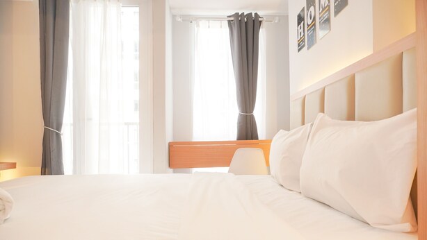 A hotel room with a large bed, a wooden headboard, and a window with curtains. - Good Choice And Cozy Studio At Tokyo Riverside Pik 2 Apartment (Teluknaga)