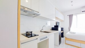 A modern kitchen with a gas stove, sink, and white cabinets. There is a small refrigerator and a window with curtains. - Best Deal And Homey Studio Sky House Alam Sutera Apartment (Tangerang)