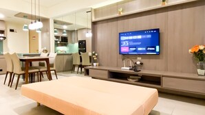 Une chambre d’hôtel moderne dotée d’un grand lit, d’un coin repas avec des chaises, d’une cuisine à l’arrière-plan et d’un téléviseur fixé au mur, qui diffuse différents services de diffusion en continu.