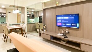 Un salon moderne avec un téléviseur à écran plat fixé au mur, un coin repas avec une table et des chaises, et une cuisine en arrière-plan.