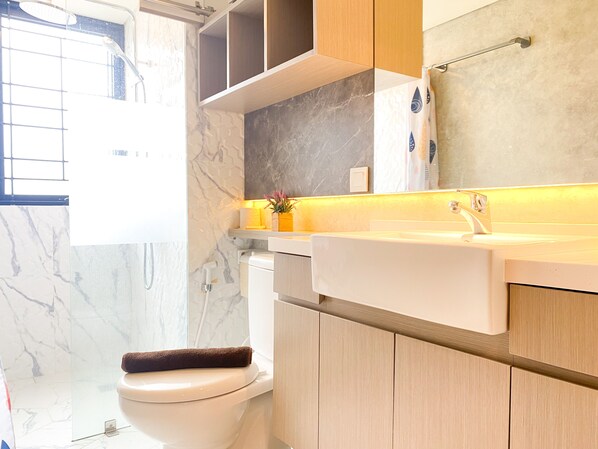 Bathroom features a white toilet, sink, and shower with a glass door, along with a shelf and a vase of flowers.