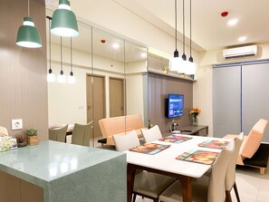 A modern hotel room with a dining area, a flat-screen TV, and a large mirror. - Well Furnished And Comfort 3Br Meikarta Apartment (Cikarang)