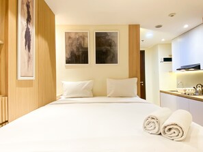Cozy retreat with a neatly made bed, minimalist decor, and a fully equipped kitchen area.
