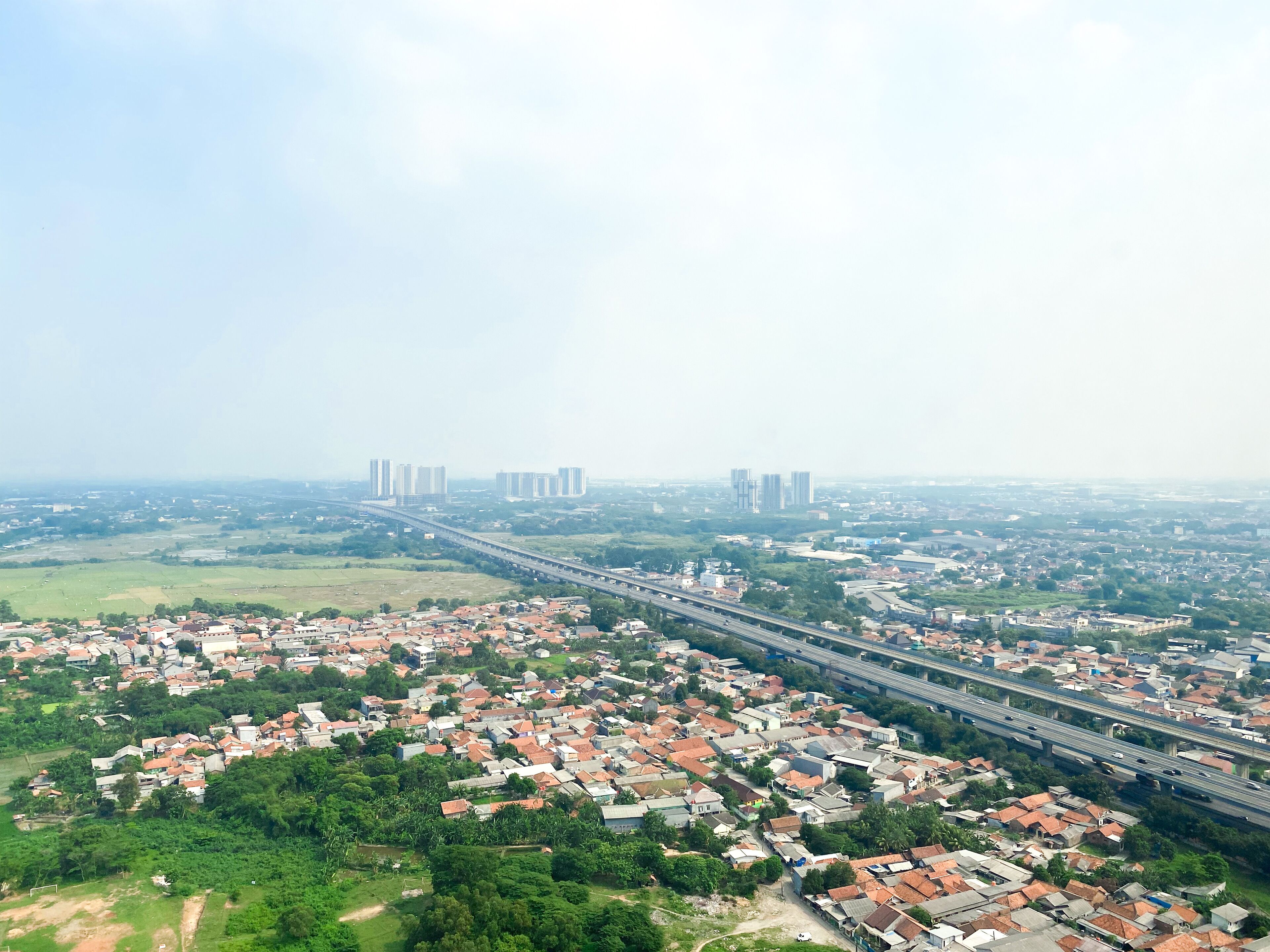 Vista aérea de una ciudad con un puente destacado, zonas residenciales y rascacielos a lo lejos.