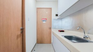A narrow hallway with a wooden door, a sink with a faucet, and a tiled floor. - Good Deal And Homey Studio Apartment At B Residence (Pagedangan)