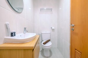 A small, clean bathroom with a white sink, toilet, and a wooden door.