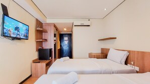 Habitación de hotel con dos camas, un televisor en la pared, un escritorio y una puerta que da al baño.
