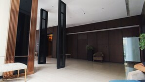 A modern lobby with a white bench, dark wooden panels, and a glass partition. - Good Choice And Homey 1Br Grand Sungkono Lagoon Apartment (Surabaya)