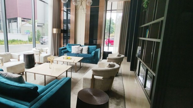 A modern interior with a blue sofa set, a white coffee table, and a beige armchair. Large windows offer a view of the street outside. - Good Choice And Homey 1Br Grand Sungkono Lagoon Apartment (Surabaya)